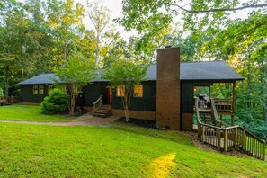 A two-story house with a brick chimney, a wooden deck, and a covered porch. - 5 BR, 3 King Beds, Fire Pit, Hot Tub, Game room! Amazing Year Round Lake View!! (Sparta)