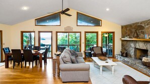 A spacious living room with a fireplace, a dining area with a wooden table and chairs, and large windows offering views of the outdoors. - 5 BR, 3 King Beds, Fire Pit, Hot Tub, Game room! Amazing Year Round Lake View!! (Sparta)