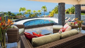 Un espace aménagé au bord de la piscine, avec des meubles en osier, une vue sur l’océan et des plantes tropicales.