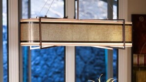 Una mesa de comedor con un frutero tejido en el centro, sillas de madera y una lámpara colgante.