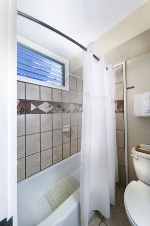 Ein Badezimmer mit Badewanne, Duschvorhang, Toilette und einem Fenster mit Jalousien.
