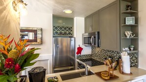 A modern kitchen with stainless steel appliances, a tiled backsplash, and a decorative mirror. - Oceanview #105 at Hana Kai Maui - Sweet Studio Unit, Great View and Decor! (Hana)