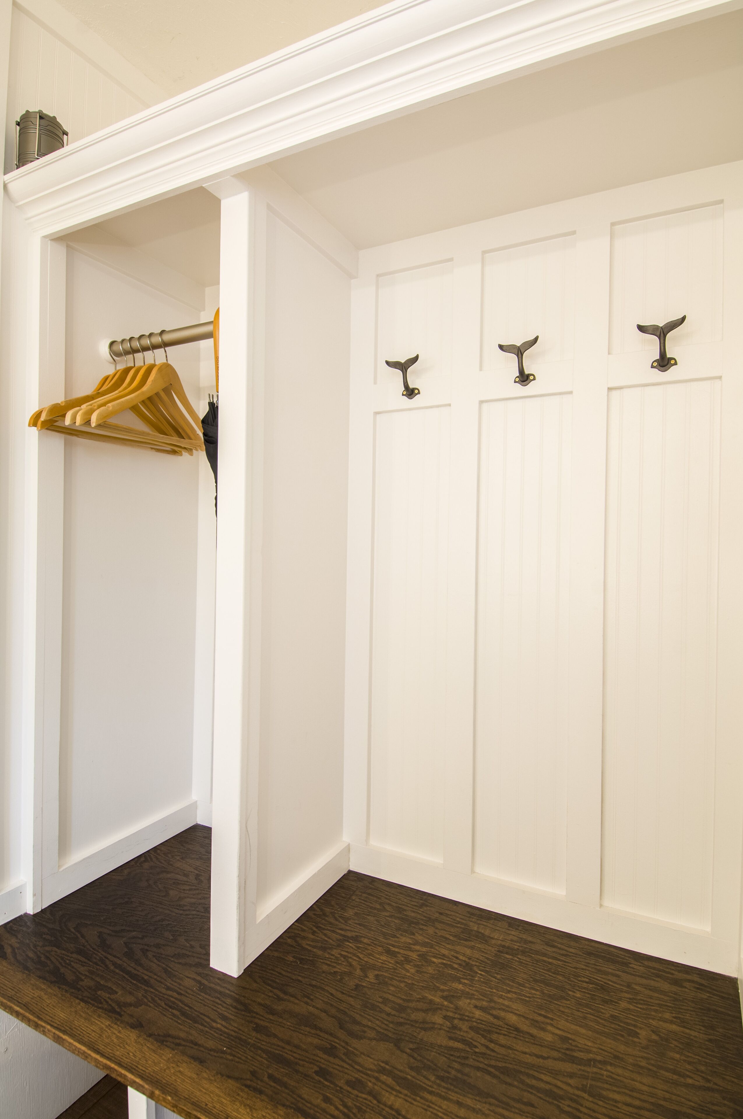 A white closet with three doors, each with a metal hook. A wooden hanger is hanging on the left side.