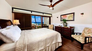 A hotel room with a bed, a ceiling fan, a desk, a chair, a dresser, and a view of the ocean. - Oceanview #105 at Hana Kai Maui - Sweet Studio Unit, Great View and Decor! (Hana)