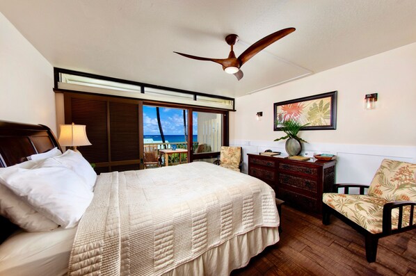 Ein Hotelzimmer mit Bett, Deckenventilator, Schreibtisch, Stuhl, Kommode und Meerblick.