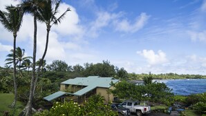 A building with a green roof, surrounded by lush greenery and palm trees, overlooking a body of water. - Oceanview #105 at Hana Kai Maui - Sweet Studio Unit, Great View and Decor! (Hana)