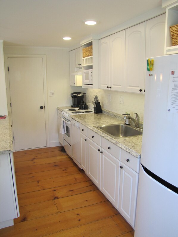 A compact kitchen with white cabinets, a stainless steel sink, a microwave, and a refrigerator. - Walk to Town! Bike or Bus to Beach! Charming Cottage- Leeward- on Private Lane (Nantucket)