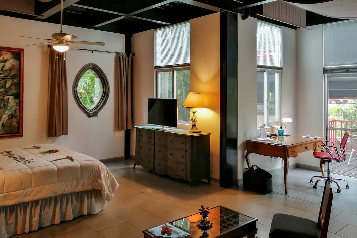 Habitación de hotel con cama, escritorio con lámpara, silla, televisor y ventana con persianas.