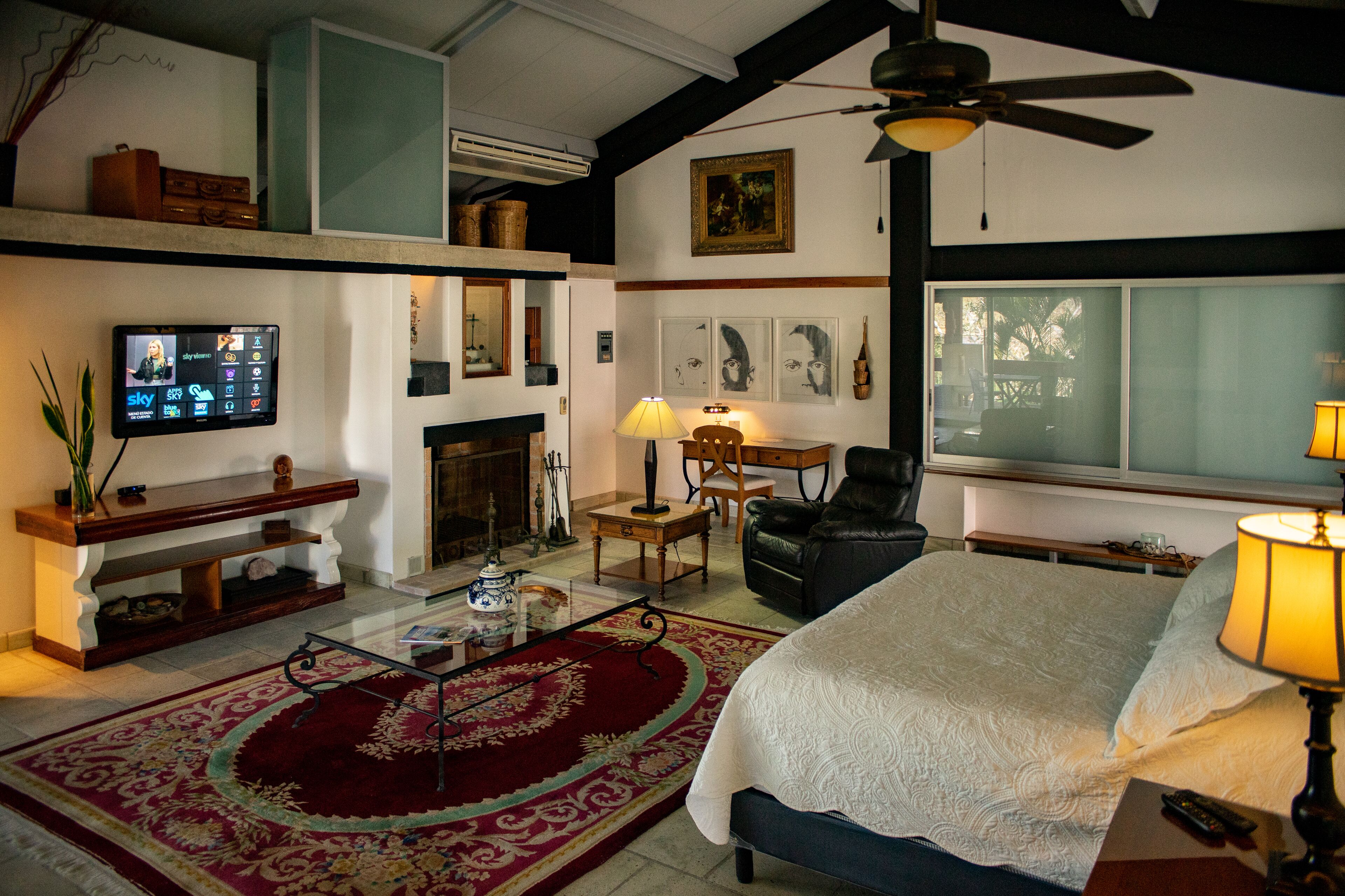 A spacious living room with a large bed, a fireplace, a television, and a ceiling fan.
