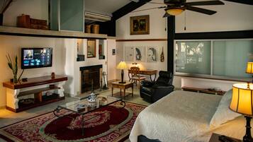 A spacious living room with a large bed, a fireplace, a television, and a ceiling fan.