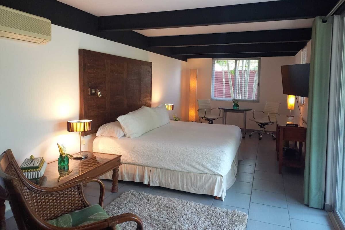 Una habitación de hotel con una cama grande, un escritorio, una silla, un televisor y una ventana con persianas.