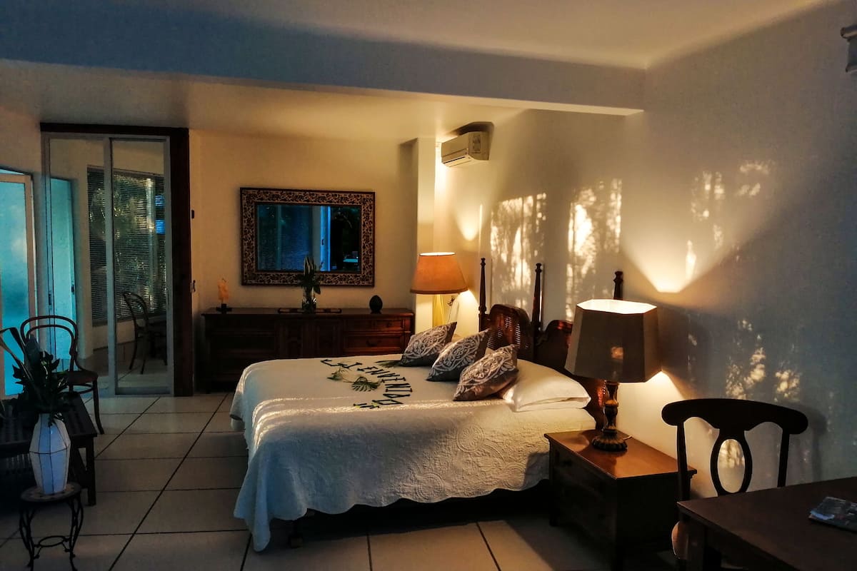 Un dormitorio con cama, lámparas de noche, cómoda, espejo y ventana.