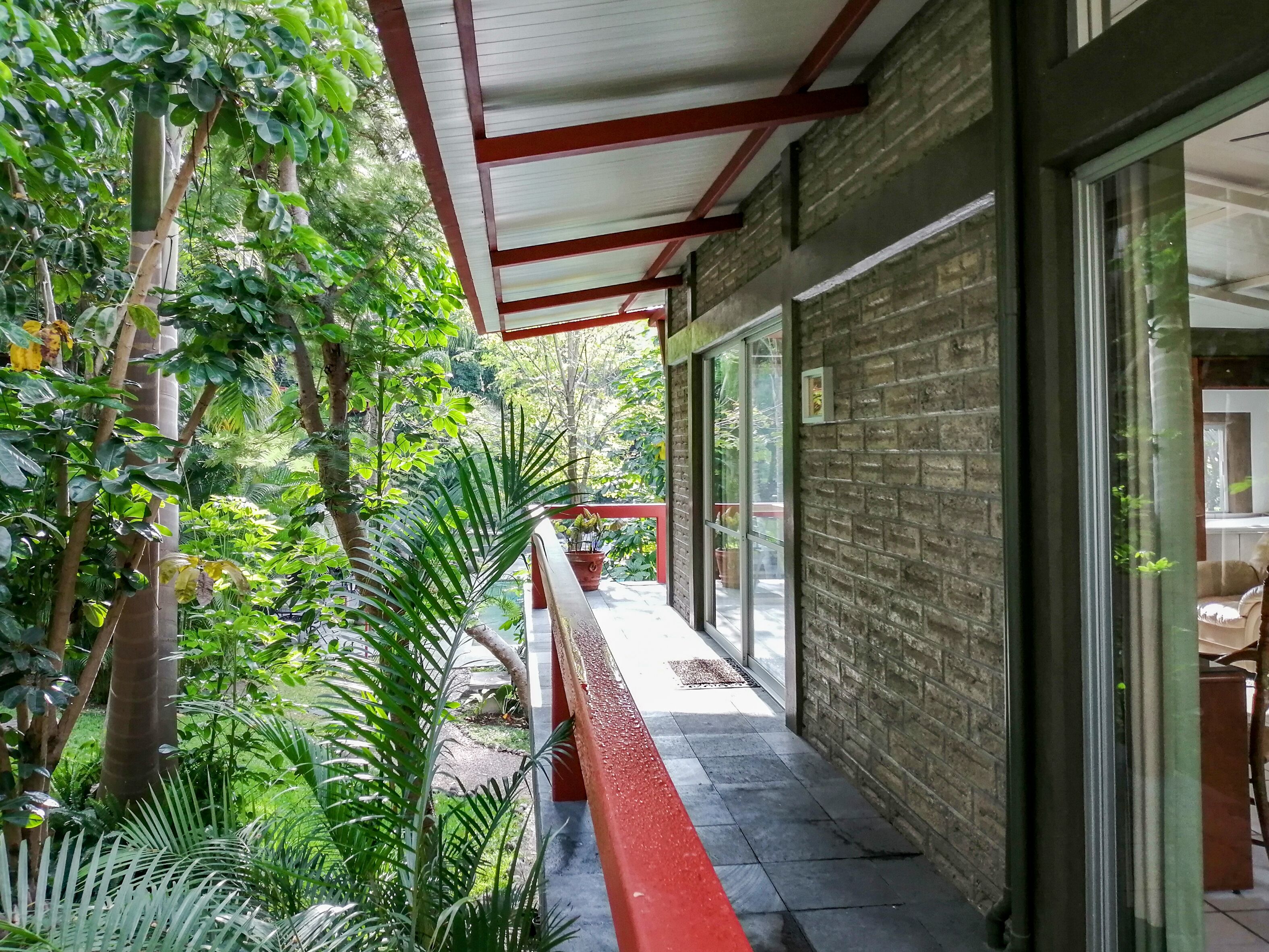 A covered outdoor area with a brick wall, potted plants, and a red railing.