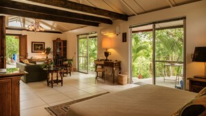 Una habitación amplia con una cama grande, un comedor y vistas a exuberante vegetación a través de grandes puertas correderas.