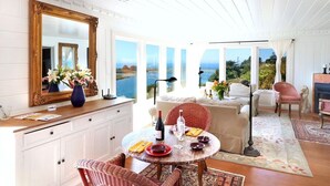 Ein Essbereich mit einem runden Tisch, Stühlen und Blick aufs Meer.
