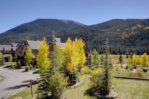 A lodge with a mountain backdrop, featuring a parking area and a well-maintained lawn with trees.
