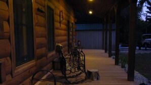 Een houten hutje met een veranda, een metalen leuning en een stapel hout.