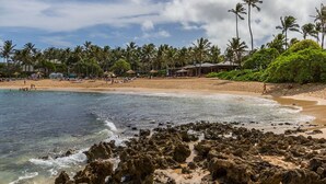 Une plage avec une eau cristalline, un rivage rocheux, des palmiers et des parasols de plage.