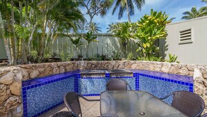 Un espace aménagé au bord de la piscine, avec un mur en pierre, une piscine aux carreaux bleus et du mobilier d’extérieur.