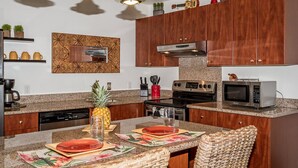 Une cuisine moderne avec des meubles en bois, des plans de travail en granit, une cuisinière encastrée, un four à micro-ondes et un coin repas avec une table dressée pour deux personnes.