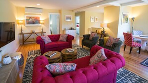 A living room with a red sofa, a grey armchair, and a coffee table. There are two lamps, a rug, and a painting on the wall. - Napa Valley Retreat in Calistoga! (Calistoga)