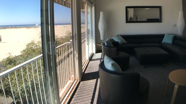 Ein Wohnzimmer mit einer großen Eckcouch, einer Stehlampe und Blick auf den Strand.