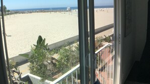 Blick auf einen Strand vom Balkon aus, mit blauem Himmel, Sandstrand und Personen in der Ferne.