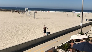 Ein Strand mit einem Rettungsturm, Sonnenschirmen und einem wolkenlosen Himmel.