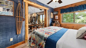 Un dormitorio con cama, ventilador de techo, ventana con cortinas, puerta de madera y televisor montado en la pared.