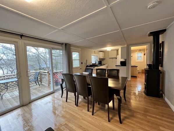 A spacious living area with a dining table, chairs, and a kitchen in the background. - Muskoka - The Hummingbird Tea Lake cabin (Coldwater)