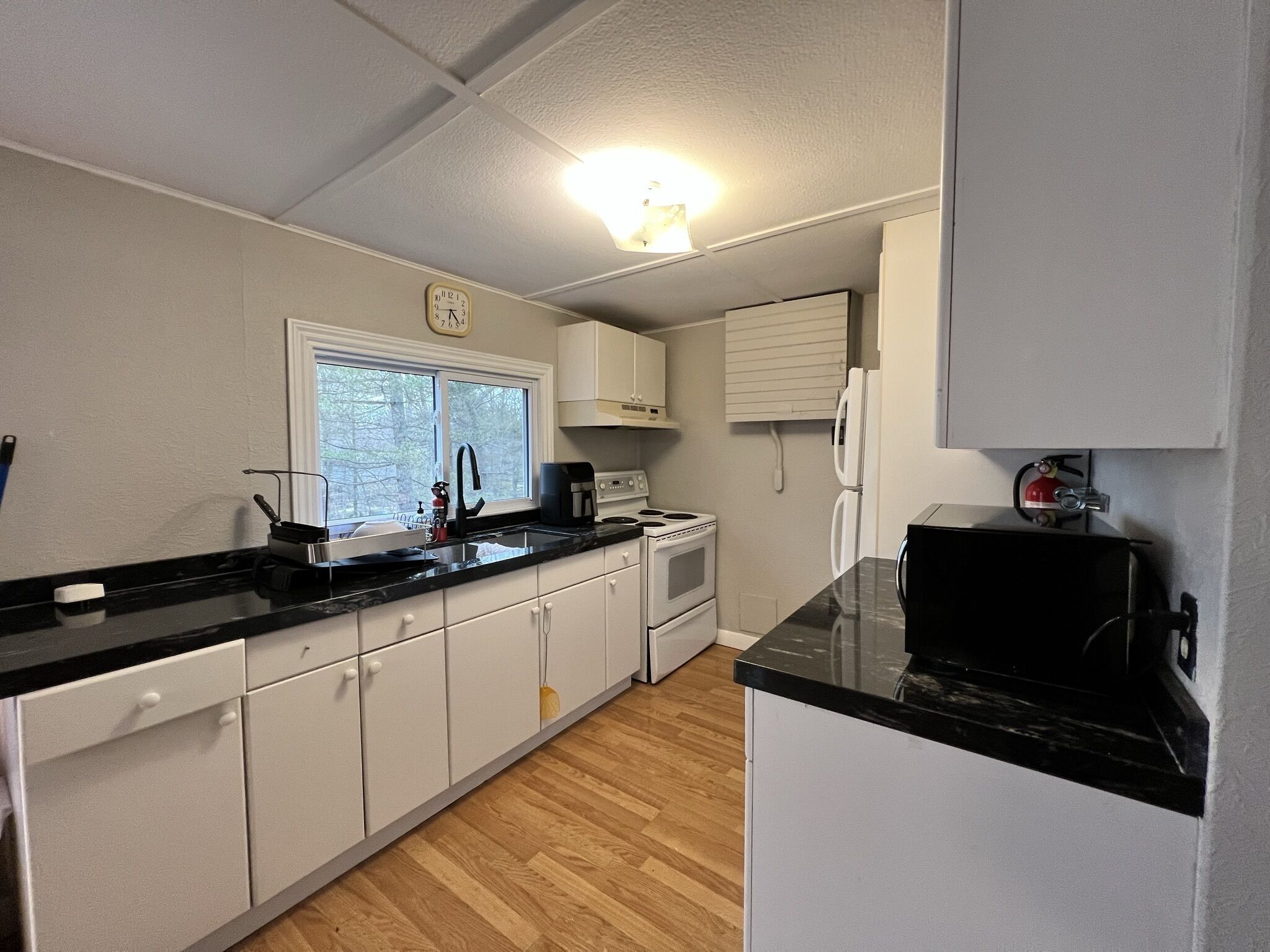 A compact kitchen with white cabinets, a black countertop, a stove, a sink, and a window.
