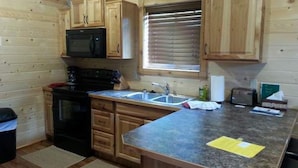 A kitchen with wooden cabinets, a stove, a microwave, a sink, and a window with blinds. - 14 miles to Yellowstone entrance. Private HOT TUB.    (Island Park)