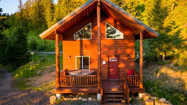 A wooden cabin with a porch, a door, and a small deck. - 14 miles to Yellowstone entrance. Private HOT TUB.    (Island Park)