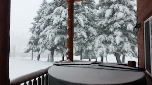 A wooden cabin with a snow-covered deck and a view of snow-laden trees. - 14 miles to Yellowstone entrance. Private HOT TUB.    (Island Park)