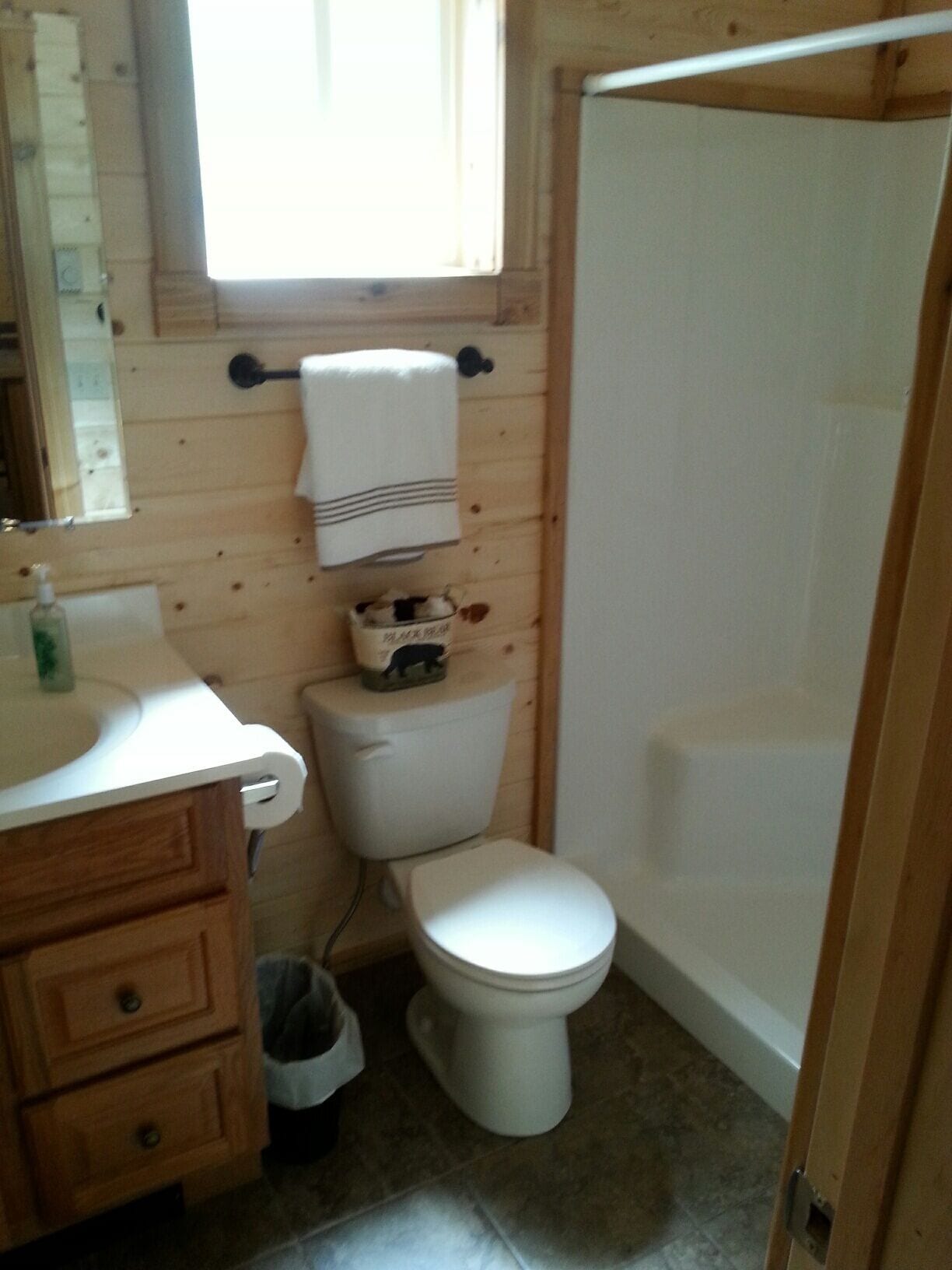 A small, compact bathroom with a wooden interior, a toilet, a sink, and a shower.