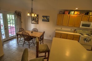 Una cocina con armarios de madera, un microondas y una estufa. Hay una mesa de comedor con sillas y una araña.