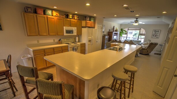 A modern kitchen with wooden cabinets, a large island with stools, a microwave, and a refrigerator. - Pet-Friendly Island Retreat | No Weight/Breed Limits | 1mi Clayton’s Beach Bar (South Padre Island)