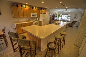 A modern kitchen with wooden cabinets, a large island with stools, a microwave, and a refrigerator.