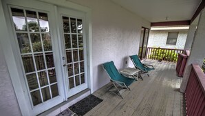 A covered porch with wooden flooring, two green folding chairs, and a red railing. - Pet-Friendly Island Retreat | No Weight/Breed Limits | 1mi Clayton’s Beach Bar (South Padre Island)