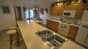 A modern kitchen with a central island, stainless steel sink, wooden cabinets, and a microwave. - Pet-Friendly Island Retreat | No Weight/Breed Limits | 1mi Clayton’s Beach Bar (South Padre Island)