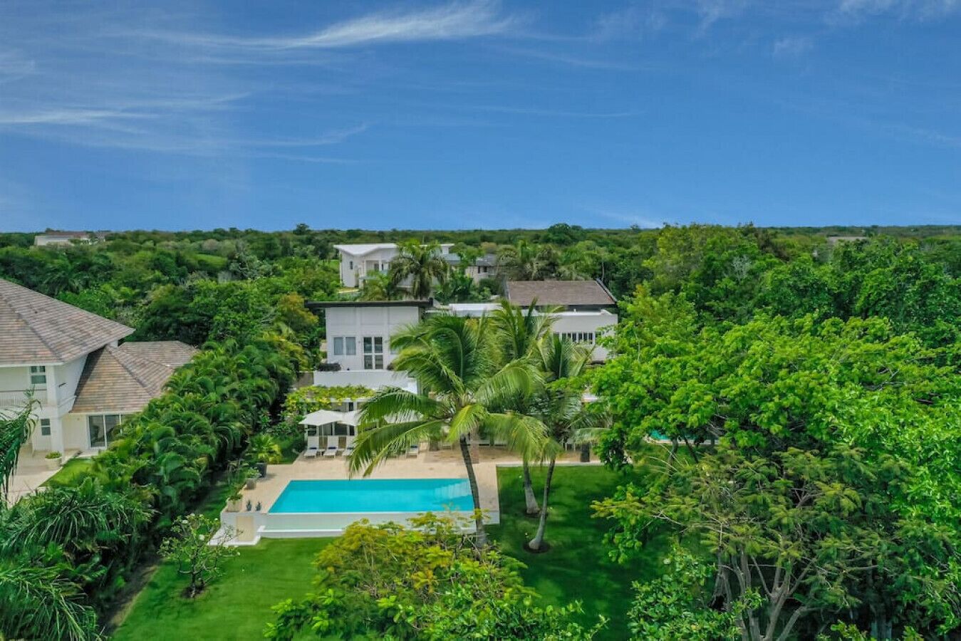 Une grande maison avec une piscine, entourée d’une végétation luxuriante et de palmiers.