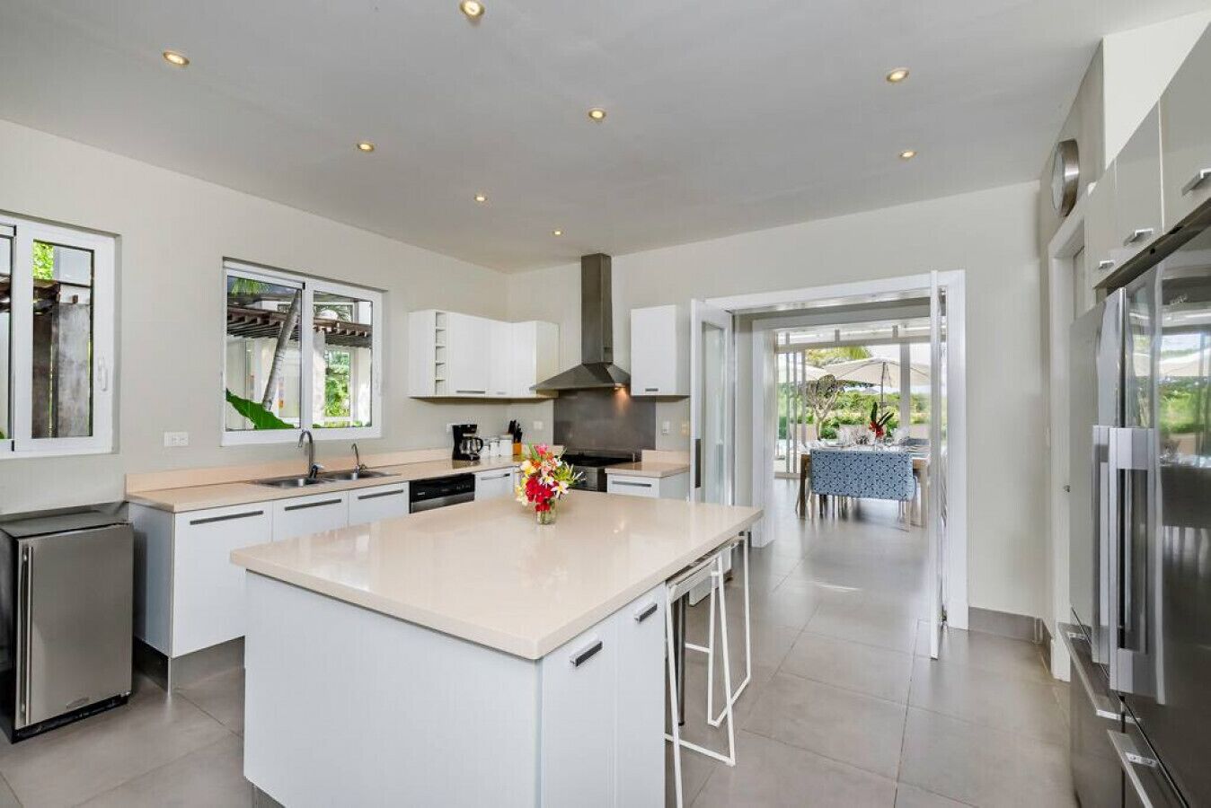 Une cuisine moderne avec des meubles blancs, un îlot central et une vue sur un espace de repas extérieur.