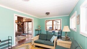 A cozy living room with a sofa, a small table with a lamp, and a view of the outside through a window. - Chalet In West Virginia on the Cacapon River. Sleeps 8 (Great Cacapon)