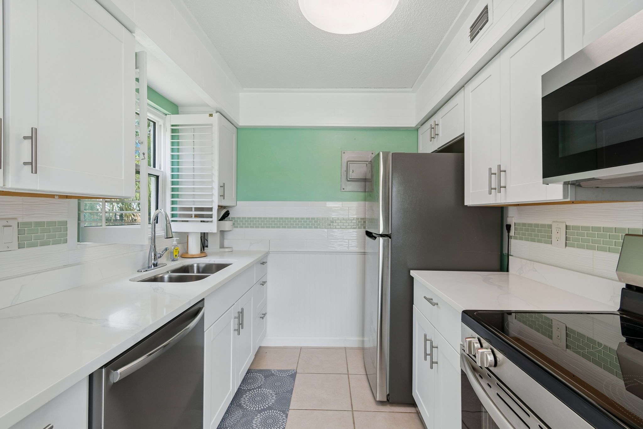 A modern kitchen with white cabinetry, a stainless steel refrigerator, a microwave, and a built-in oven.