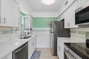 A modern kitchen with white cabinetry, a stainless steel refrigerator, a microwave, and a built-in oven.