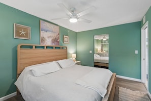 A bedroom with a bed, a nightstand, a ceiling fan, and a wall with artwork.