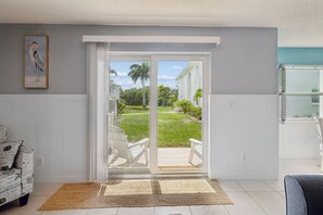 Habitación con puerta corrediza de vidrio que da a un patio exterior con una silla blanca y una mesita.