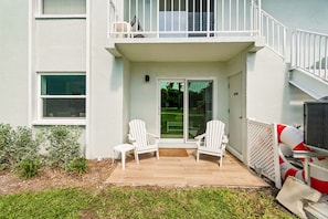 A residential building with a balcony, two white chairs, a sliding glass door, and a small garden area.