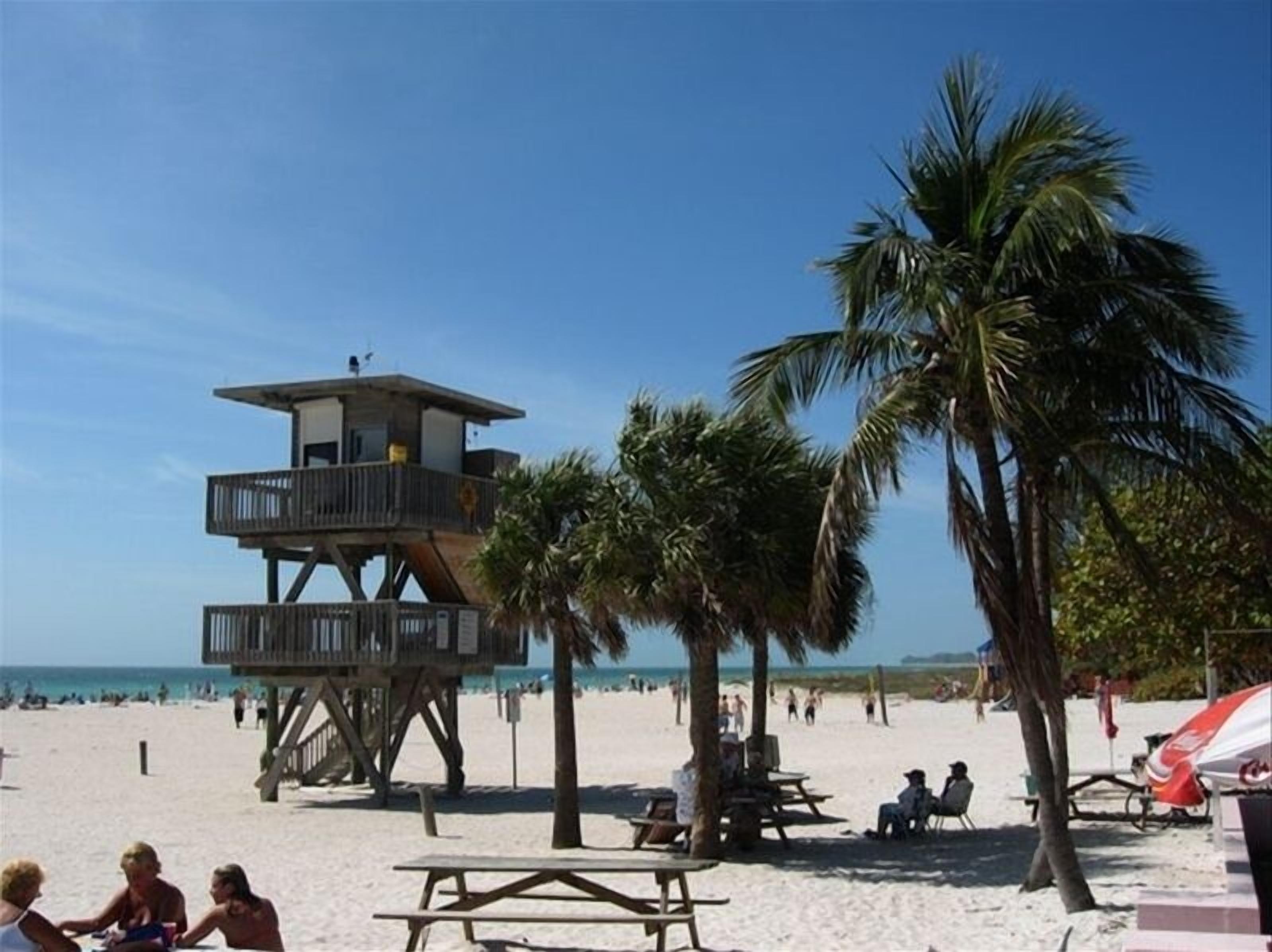 Une tour de surveillance sur une plage, avec des palmiers et des tables de pique-nique.