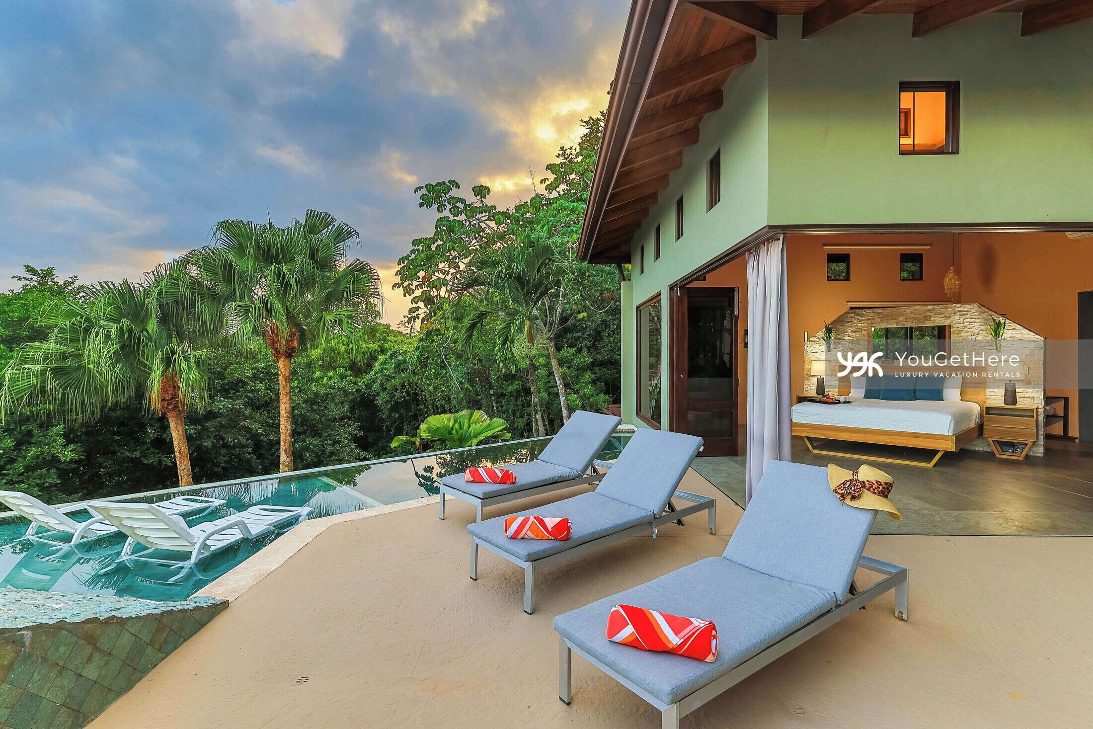 A modern villa with a pool, lounge chairs, and a bedroom with a large bed and a stone fireplace.